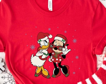 May include: Red t-shirt with a Christmas-themed graphic of Mickey Mouse and Minnie Mouse wearing Santa hats. The graphic shows Mickey Mouse wearing sunglasses and Minnie Mouse holding a present.