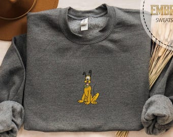 May include: A charcoal gray sweatshirt with an embroidered Pluto design. The cartoon dog is sitting with a yellow body, black ears, and a yellow collar. The sweatshirt has long sleeves and a crew neck. A brown hat is in the background.