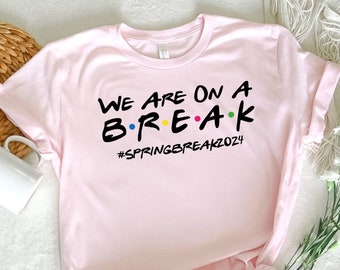 May include: Pink t-shirt with the text "We are on a B.R.E.A.K #SpringBreak2024" in black with colorful dots.