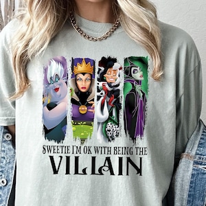 Pu&ograve; includere: T-shirt verde chiaro con quattro personaggi di cattivi dei cartoni animati in pannelli verticali. Il testo "Sweetie I'm OK with being the Villain" &egrave; stampato sotto in nero.