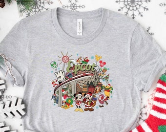 May include: Gray t-shirt with a colorful graphic of the Epcot theme park, featuring Mickey Mouse and other Disney characters. The graphic includes the text "Epcot" and a festive holiday theme.