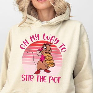 May include: A beige hoodie with a pink and white graphic of a cartoon mouse holding a stack of cheese. The graphic says "On my way to stir the pot".