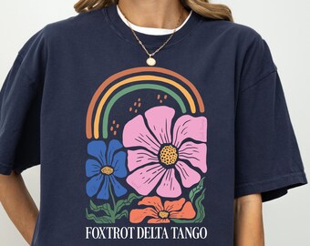 May include: A navy blue t-shirt with a graphic of colorful flowers and a rainbow. The text "FOXTROT DELTA TANGO" is printed below the graphic.
