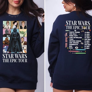 May include: A navy blue sweatshirt with a graphic print of Star Wars characters on the front and a list of Star Wars characters and their appearance dates on the back. The text on the front reads "Star Wars The Epic Tour". The text on the back reads "Star Wars The Epic Tour" and lists characters such as Darth Vader, Han Solo, Boba Fett, Luke Skywalker, Yoda, Obi-Wan Kenobi, Leia Organa, Chewbacca, R2D2, and BB8.