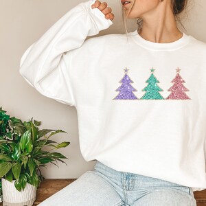 May include: White sweatshirt with a design of three glitter Christmas trees in purple, teal, and pink.