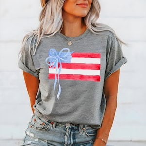 May include: A grey t-shirt with a watercolour design of an American flag with a blue bow on top.