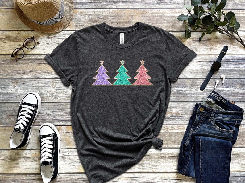 May include: A dark grey t-shirt with a design of three glitter Christmas trees in purple, teal, and pink.