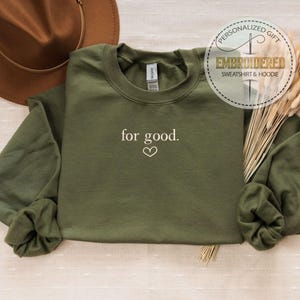 May include: A green sweatshirt with the text "for good." embroidered in white on the front. A small heart is embroidered below the text.