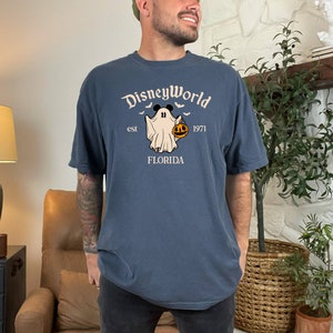 May include: A dark blue t-shirt featuring a white graphic of a ghost holding a jack-o-lantern. The text "DisneyWorld est 1971 FLORIDA" is printed on the shirt.