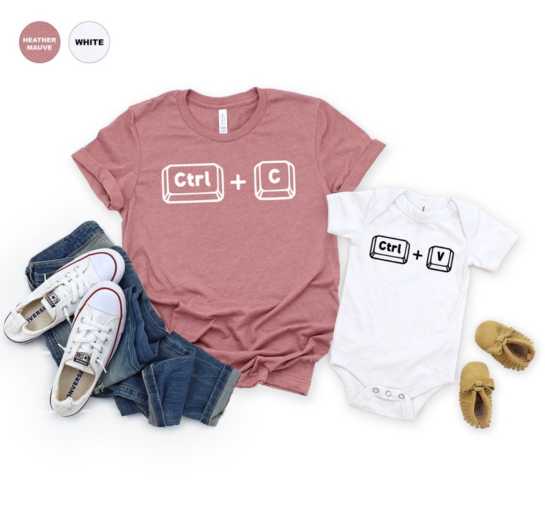 May include: A heather mauve t-shirt with the text "Ctrl + C" in white, and a white bodysuit with the text "Ctrl + V" in black. The t-shirt is paired with blue jeans and white sneakers.