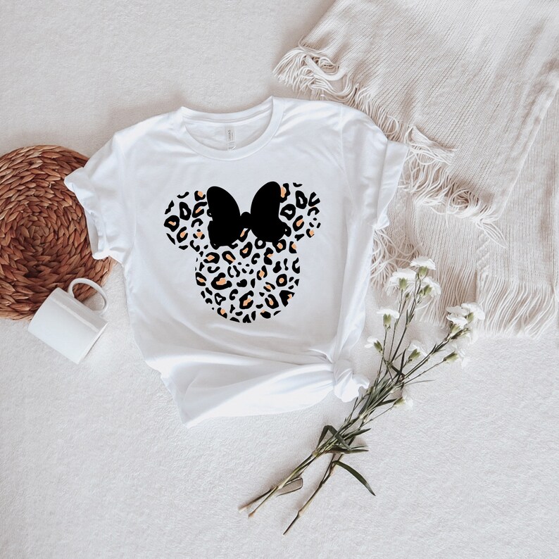 May include: White t-shirt with a black and orange leopard print Minnie Mouse head design. The bow is black.