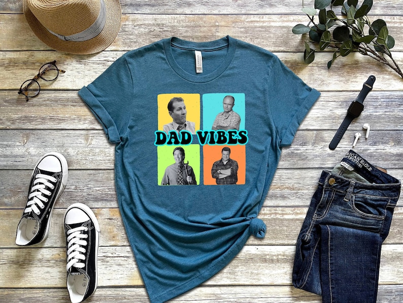 May include: Teal blue t-shirt featuring a graphic of four men in black and white photographs. The photos are in squares with coloured backgrounds. The text "DAD VIBES" is in a retro font.