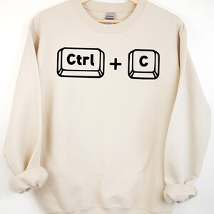 May include: A beige sweatshirt with a black graphic of the computer keys "Ctrl" and "C" printed on the front.