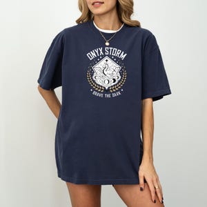 May include: A navy blue oversized t-shirt with a graphic print of a dragon in a circle with the text "ONYX STORM" above and "BRAVE THE DARK" below.