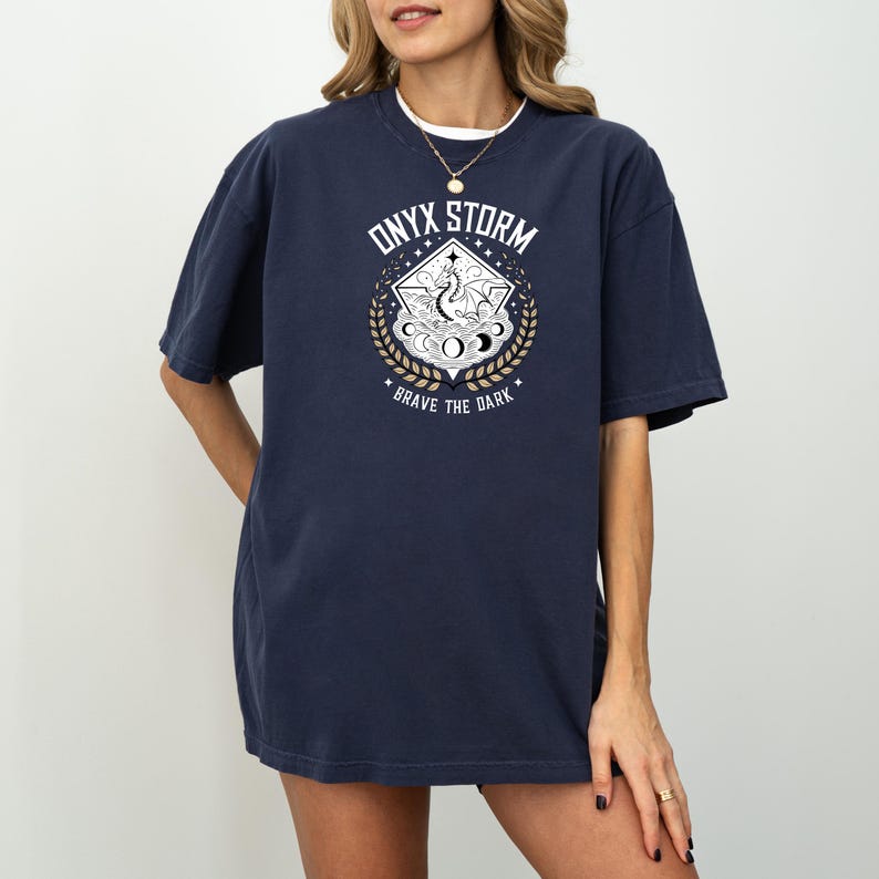 May include: A navy blue oversized t-shirt with a graphic print of a dragon in a circle with the text "ONYX STORM" above and "BRAVE THE DARK" below.
