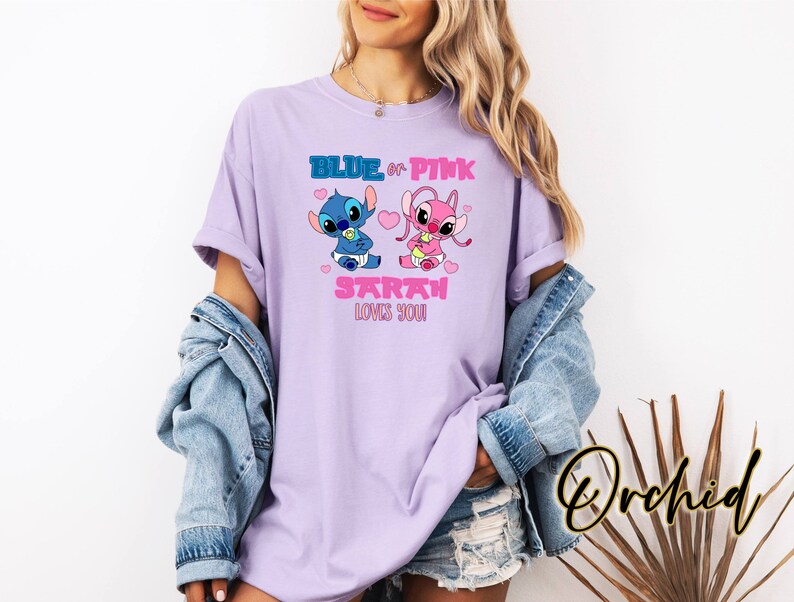 May include: A lilac-colored t-shirt featuring cartoon characters Stitch and Angel, with the text "BLUE or PINK SARAH LOVES YOU!" in blue and pink. The design includes hearts and baby-themed elements. The shirt is part of a clothing collection.