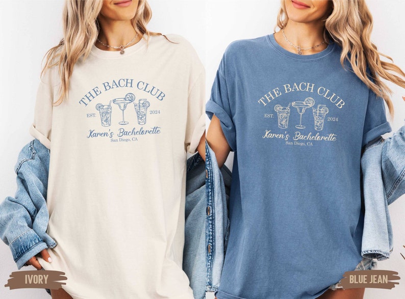 Puede incluir: Dos camisetas con un dise&ntilde;o gr&aacute;fico azul que dice "The Bach Club Est. 2024 Karen's Bachelorette San Diego, CA" con un dibujo de tres vasos de c&oacute;ctel. La camiseta de la izquierda es de color marfil y la camiseta de la derecha es de color azul vaquero.