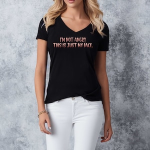 May include: A black v-neck t-shirt with the text "I'm not angry. This is just my face." in a pink and white gradient.