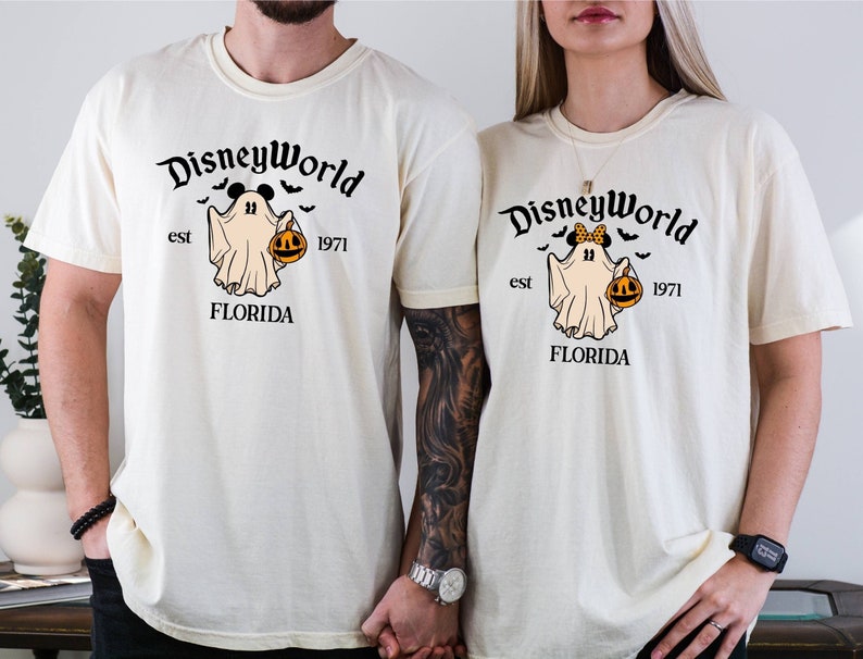 May include: Two cream coloured t-shirts with a ghost holding a jack-o-lantern. The text on the shirts reads "Disney World est 1971 Florida" with a Mickey Mouse head on the ghost.