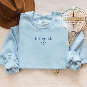 May include: A light blue sweatshirt with the text "for good." embroidered in dark blue with a small heart below the text.