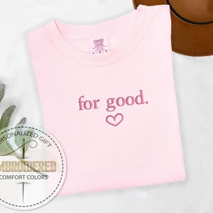May include: Pink t-shirt with the text "for good." embroidered in pink with a small pink heart below the text.