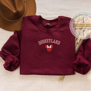 May include: Burgundy sweatshirt with the text "DISNEYLAND" in white with a red and white Mickey Mouse silhouette.