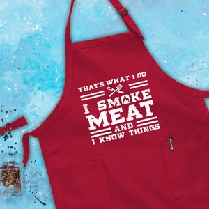 May include: Red apron with a white graphic that says "That's what I do I smoke meat and I know things".