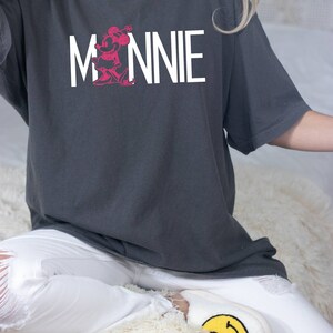May include: A gray oversized t-shirt with a white graphic of Minnie Mouse and the word "MINNIE" printed on the front.