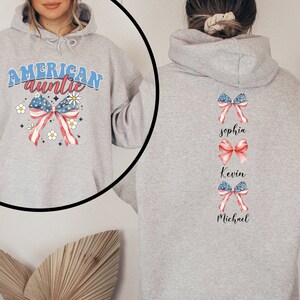 May include: Gray hooded sweatshirt with the text "American auntie" and a red, white, and blue bow with stars and white daisies. The back of the sweatshirt has three red, white, and blue bows with the names "Sophia", "Kevin", and "Michael" written below each bow.