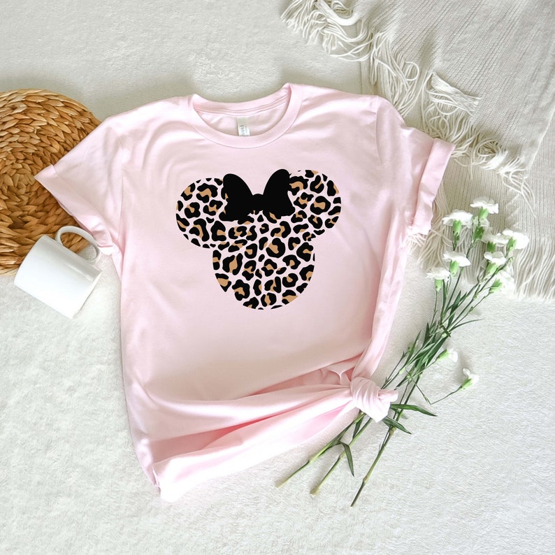 May include: A pink t-shirt with a leopard print Minnie Mouse head design. The ears and bow are black.