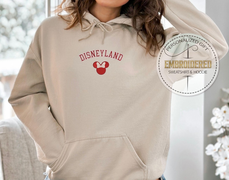 May include: A beige hoodie with a red embroidered Mickey Mouse head and the text "DISNEYLAND" in red.