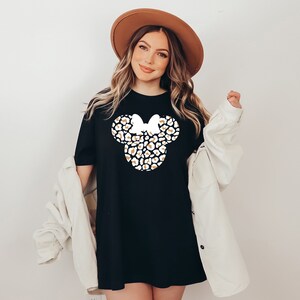 May include: A black t-shirt with a white and gold leopard print Minnie Mouse head design. The shirt is oversized and has a relaxed fit.