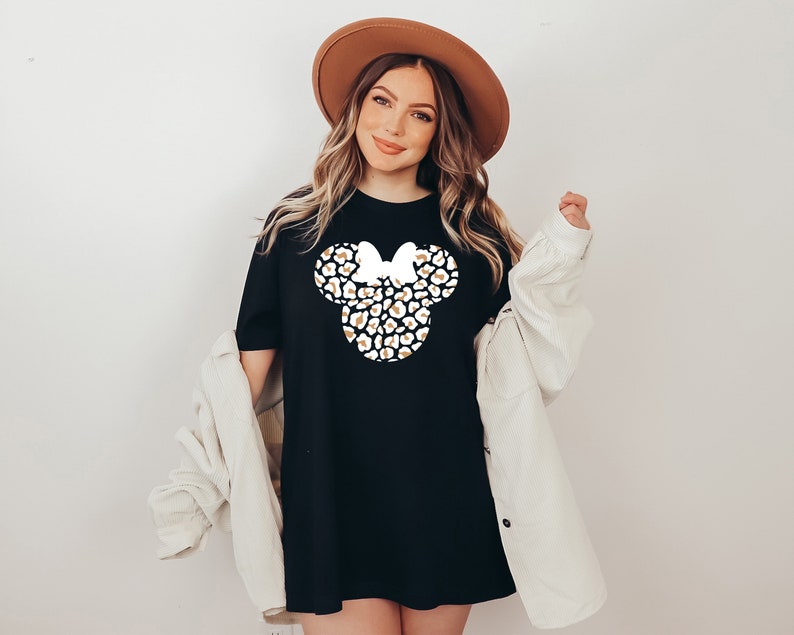 May include: A black t-shirt with a white and gold leopard print Minnie Mouse head design. The shirt is oversized and has a relaxed fit.
