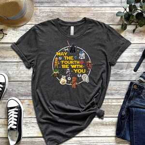 以下が含まれることがあります： スターウォーズのキャラクターと「May the Fourth Be With You」というテキストが描かれた黄色の円形グラフィックが施されたダークグレーのTシャツです。