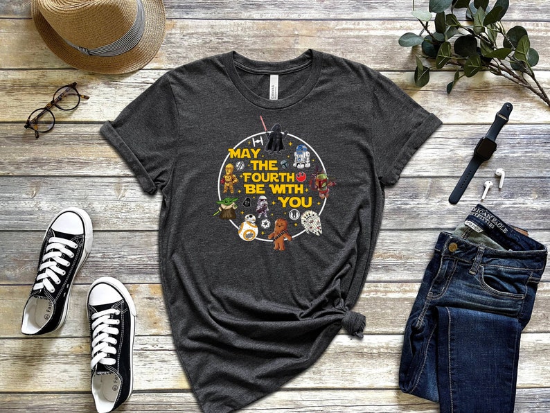 以下が含まれることがあります： スターウォーズのキャラクターと「May the Fourth Be With You」というテキストが描かれた黄色の円形グラフィックが施されたダークグレーのTシャツです。