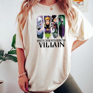 Pu&ograve; includere: T-shirt color crema con un disegno di quattro cattivi dei cartoni animati, tra cui Ursula, la Regina Cattiva, Crudelia De Mon e Malefica. Il testo sulla maglietta dice "Sweetie I'm OK with being the Villain".
