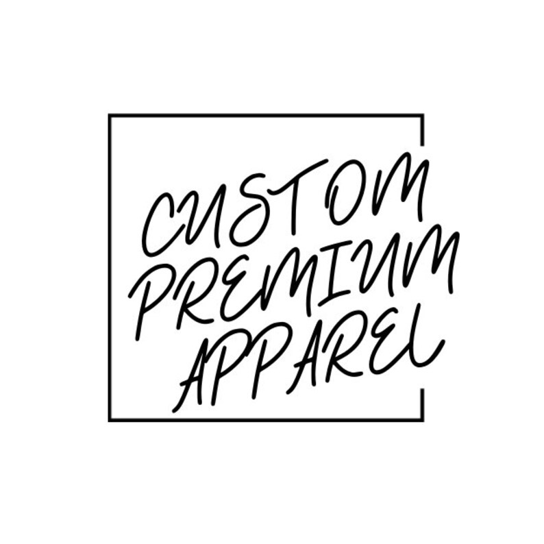 May include: Black and white graphic with the words "CUSTOM PREMIUM APPAREL" in a handwritten style font, enclosed within a black square border. The background is plain white.