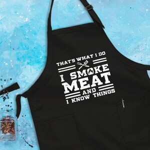 May include: Black apron with white text that reads "That's what I do I smoke meat and I know things". The text is surrounded by white lines. There is a small pocket on the right side of the apron.