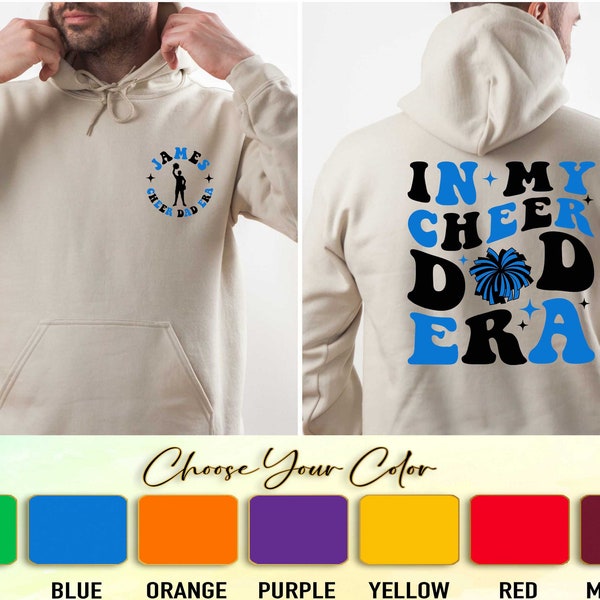 May include: A beige hoodie with a blue and black graphic on the back that says "In My Cheer Dad Era" and a blue and black graphic on the front that says "James Cheer Dad Era". The hoodie is available in green, blue, orange, purple, yellow, red, and maroon.
