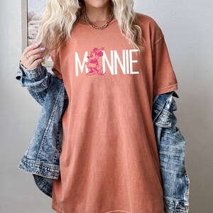 May include: A rust-colored oversized t-shirt with a white graphic of Minnie Mouse and the word "MINNIE" in white letters.