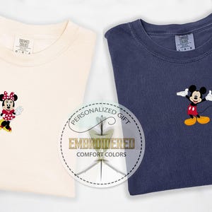May include: Two t-shirts with embroidered Disney characters. The left shirt is cream colored with a red and white polka dot Minnie Mouse. The right shirt is navy blue with a red and yellow Mickey Mouse. Both shirts have the text "Personalized Gift Embroidered Comfort Colors" on a white circle.