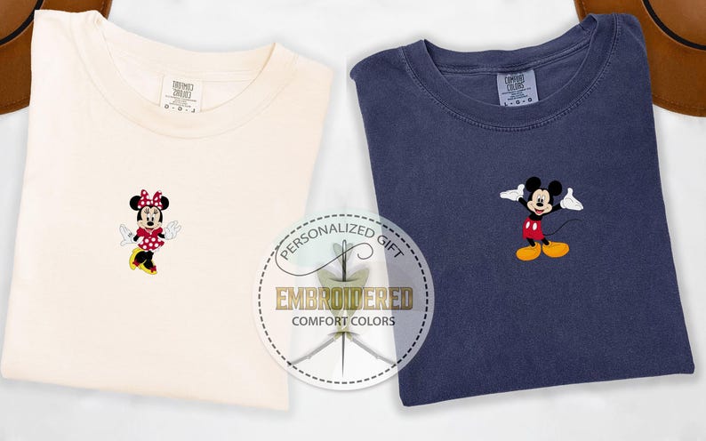 May include: Two t-shirts with embroidered Disney characters. The left shirt is cream colored with a red and white polka dot Minnie Mouse. The right shirt is navy blue with a red and yellow Mickey Mouse. Both shirts have the text "Personalized Gift Embroidered Comfort Colors" on a white circle.