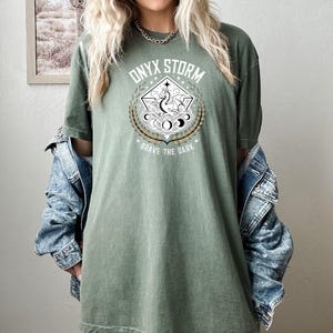 May include: A green oversized t-shirt with a graphic print of a dragon and the text "ONYX STORM" and "BRAVE THE DARK".