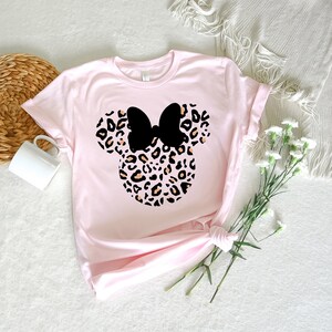 May include: A pink t-shirt with a black and brown leopard print Minnie Mouse head design.