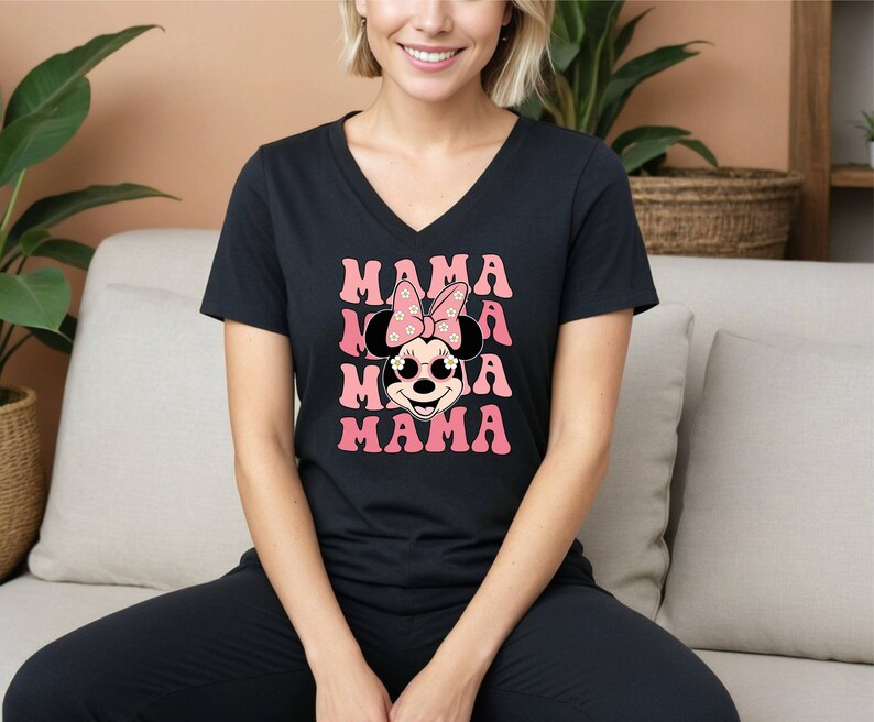 Pu&ograve; includere: Maglietta nera a collo a V con una grafica rosa e bianca di Minnie Mouse con occhiali da sole e un fiocco con fiori. Il testo "MAMA" &egrave; ripetuto quattro volte in rosa.