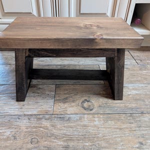 May include: A dark brown wooden step stool with a simple design. The stool has a rectangular top and a single shelf.