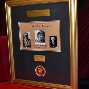 May include: A framed black and white photo of Yuri Gagarin, the first human in space, with a quote in Russian that translates to "He said: 'Let's go!'". The photo is accompanied by a small red and yellow USSR pin.