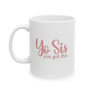 Könnte beinhalten: Weißer Keramikbecher mit gebogenem Henkel. Der Becher zeigt den Text "Yo Sis you got this" in rosa Schrift. Für heiße oder kalte Getränke.