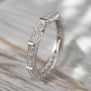 Op de afbeelding: Een zilveren bandring met een delicaat, ingewikkeld ontwerp met kleine diamanten die in het metaal zijn gezet. De ring is klassiek en elegant.