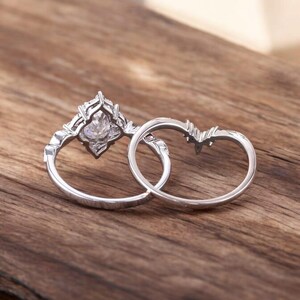 Puede incluir: Dos anillos de plata, uno con una gran piedra preciosa transparente engastada en un dise&ntilde;o decorativo e intrincado. Los anillos est&aacute;n sobre una superficie de madera.